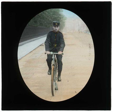 A lantern slide showing a postman on a bicycle.jpg